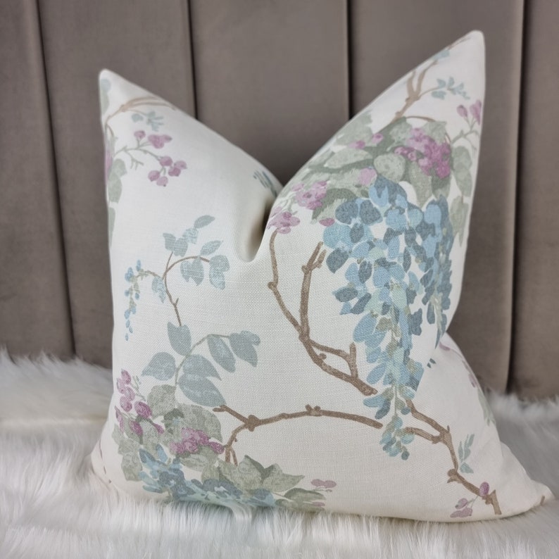 May include: A white throw pillow with a floral pattern featuring blue, green, and pink flowers. The pillow has a soft, textured fabric.
