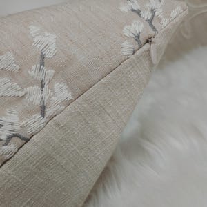 Peut inclure: Un coussin beige avec un motif floral brod&eacute; blanc et gris. Le coussin a une fermeture &eacute;clair.