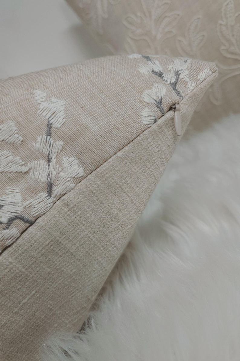 Peut inclure: Un coussin beige avec un motif floral brod&eacute; blanc et gris. Le coussin a une fermeture &eacute;clair.