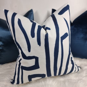 Può includere: Un cuscino bianco con un motivo geometrico astratto blu navy. Il cuscino è mostrato su una superficie di pelliccia sintetica bianca.