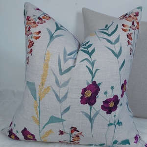 May include: A decorative cushion with a floral pattern featuring pink, purple, and yellow flowers on a light grey background.