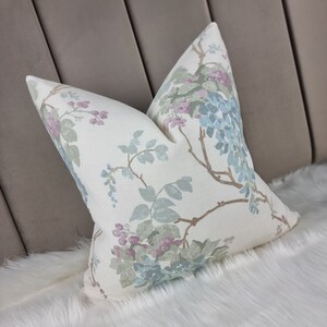 May include: A white pillow with a floral pattern featuring blue, pink, and green flowers on a white background. The pillow is on a white fluffy surface.