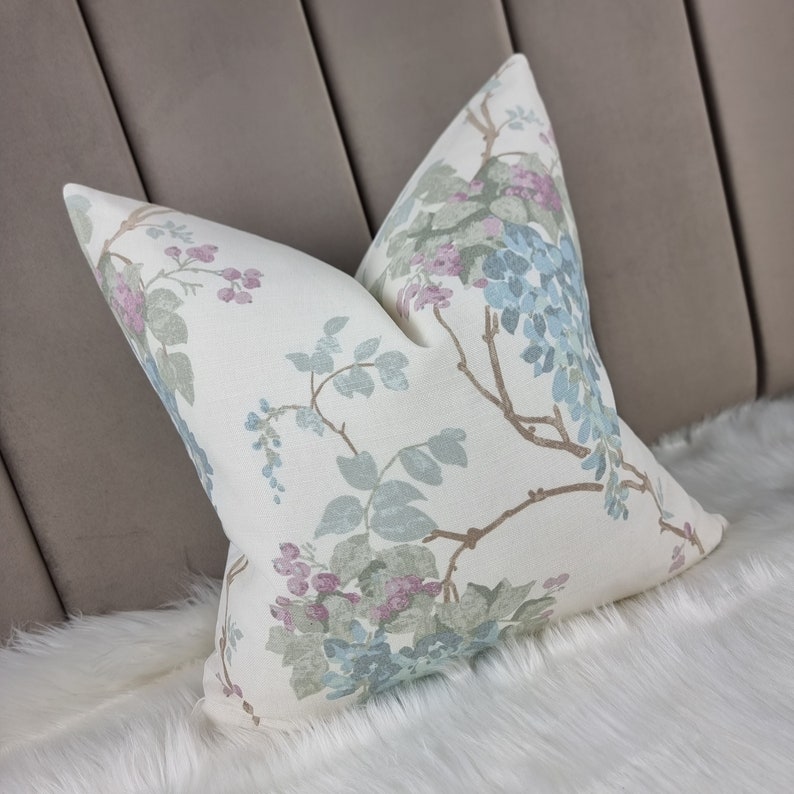 May include: A white pillow with a floral pattern featuring blue, pink, and green flowers on a white background. The pillow is on a white fluffy surface.
