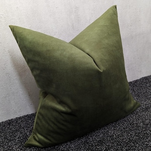 Peut inclure: Un coussin carré vert olive avec une texture douce et veloutée. L'oreiller est incliné, mettant en valeur sa forme et sa couleur. Le tissu semble avoir un léger éclat. Ce coussin décoratif convient à la décoration intérieure.