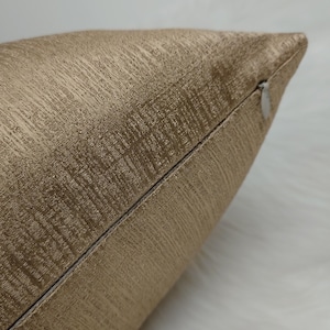 May include: Close-up of a gold pillow cover with a subtle textured pattern. The pillow cover has a zipper closure.