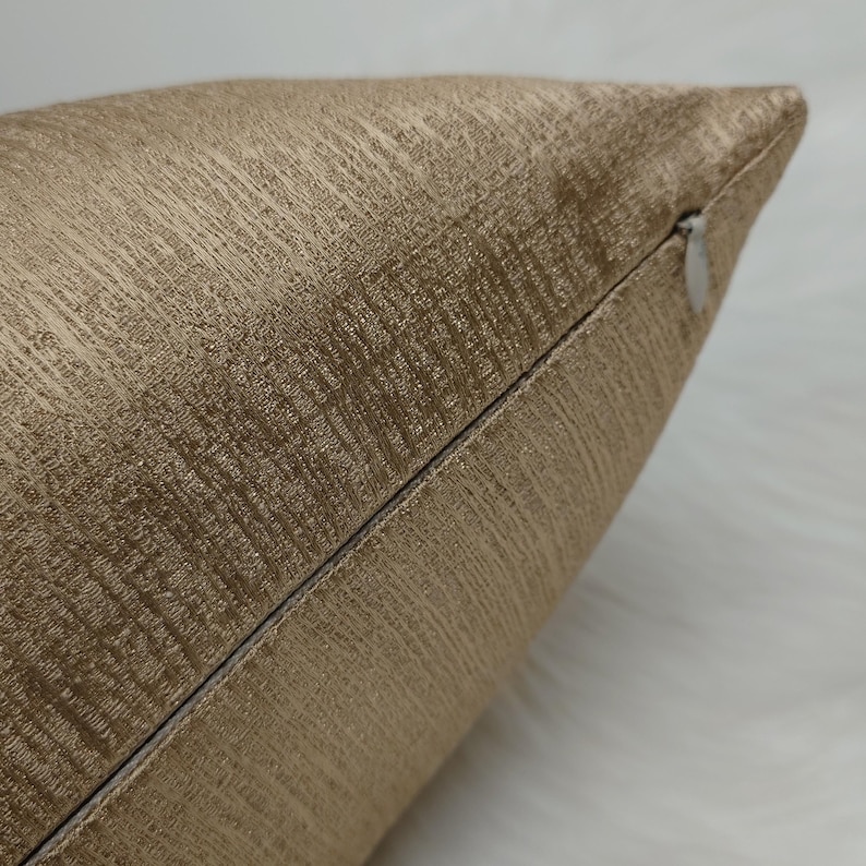 May include: Close-up of a gold pillow cover with a subtle textured pattern. The pillow cover has a zipper closure.