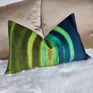 May include: A green, blue, and yellow striped throw pillow with a soft, fuzzy texture. The pillow is lying on a white, fluffy surface.