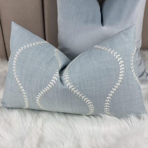 May include: A light blue throw pillow with white embroidered stitching in a curved pattern.