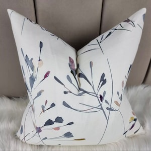 May include: White throw pillow with a floral pattern in shades of gray, pink, and yellow. The pillow has a subtle watercolor effect.