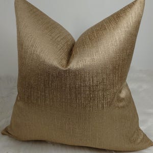 May include: A gold metallic cushion with a subtle textured pattern. The cushion is square shaped and has a soft, luxurious look.