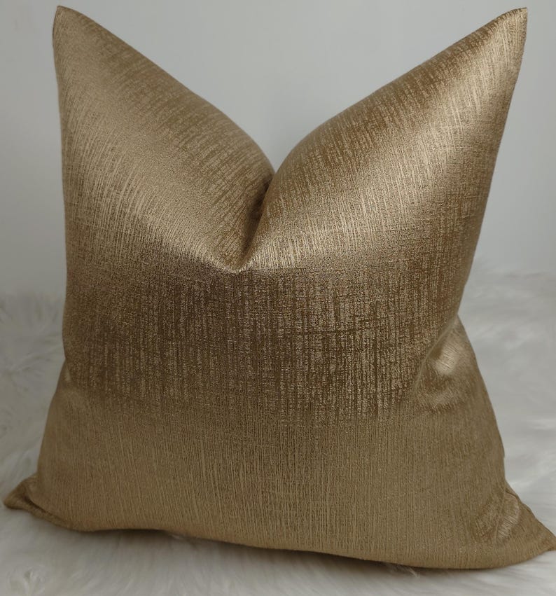 May include: A gold metallic cushion with a subtle textured pattern. The cushion is square shaped and has a soft, luxurious look.