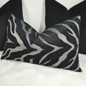 Könnte beinhalten: Zwei dekorative Kissen, eines schwarz mit silbernem Zebra-Muster und eines einfarbig schwarz.
