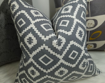 May include: Two gray and white patterned throw pillows with geometric designs. The pillows are on a white fuzzy surface.