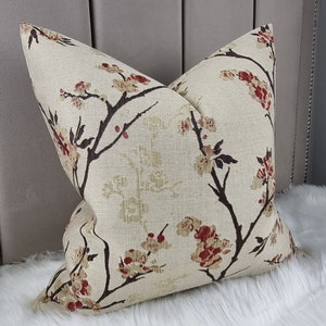 May include: A beige cushion with a floral pattern featuring brown branches and red flowers. The cushion is made of a textured fabric.