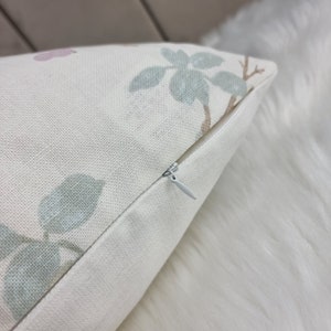 May include: A close-up of a white pillow with a zipper closure. The pillow has a floral pattern with green leaves and pink flowers.