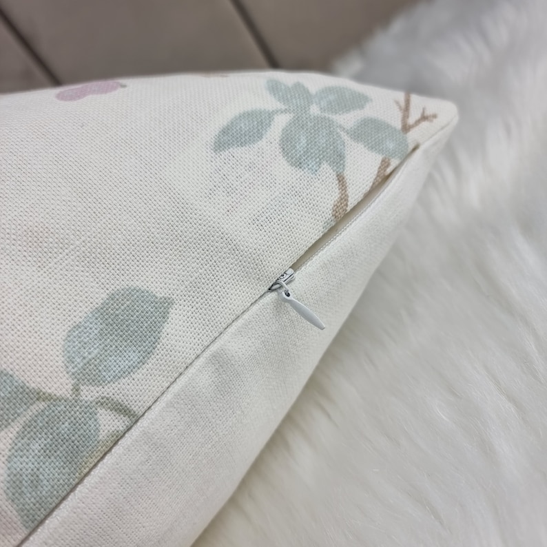 May include: A close-up of a white pillow with a zipper closure. The pillow has a floral pattern with green leaves and pink flowers.