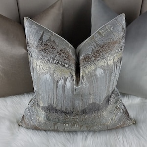 May include: A decorative throw pillow with a silver and gold abstract pattern. The pillow is made of a soft, textured fabric and has a white border.