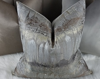 May include: A decorative throw pillow with a silver and gold abstract pattern. The pillow is made of a soft, textured fabric and has a white border.