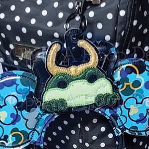 May include: Black and white polka dot backpack with a black headband with blue and green Mickey Mouse ears and a green monster charm attached.