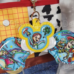 Puede incluir: Diadema de orejas de Mickey Mouse con temática de Toy Story con un fondo azul e imágenes de Woody, Jessie y Buzz Lightyear. La diadema es amarilla y blanca con un acabado brillante.
