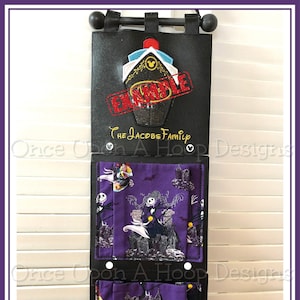 May include: A black fabric wall organizer with two pockets. The pockets are lined with purple fabric featuring a pattern of Jack Skellington and Sally from The Nightmare Before Christmas. The top of the organizer has a black leather-like fabric with a red and white ship design and the text "The Jacobs Family" in gold lettering. The word "Example" is stamped in red over the ship design.