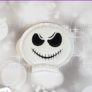 May include: White felt ghost with a black embroidered face. The ghost has a stitched smile and two black eyes. The ghost is on a white background with a sparkle effect.