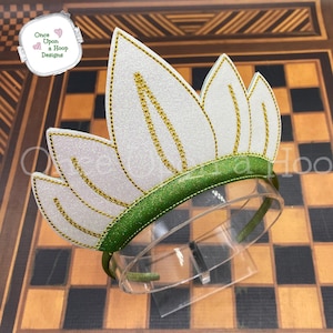 May include: A white headband with a green base and a white crown with gold accents. The crown is made of felt and has a sparkly finish.