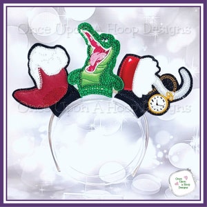 May include: A green alligator, a red boot, and a black hat with a pocket watch are attached to a clear plastic headband. The headband is decorated with glitter.