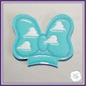 Op de afbeelding: Een turquoise blauwe strik met witte geborduurde wolken. De strik is omzoomd met witte stiksels. De tekst "Once Upon A Hoop Designs" is zichtbaar op de achtergrond.