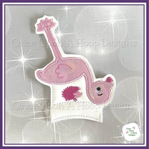 May include: Pink flamingo and hedgehog embroidery design on a white fabric background. The design is for a cup cozy or a small project.