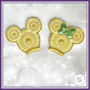 May include: Two gold glitter Mickey Mouse ears, one with a green bow. The ears are embroidered with a sunburst design.