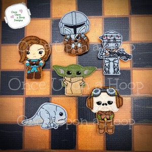 May include: A set of six embroidered felt patches featuring characters from the Star Wars franchise. The patches include a Mandalorian, a droid, a baby Yoda, a creature, a pilot, and a female character. The patches are all in different colours and have a variety of details.