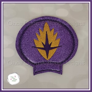 May include: Purple felt circle with a gold embroidered star-shaped design. The design is similar to the logo of the Guardians of the Galaxy.