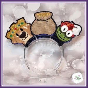 May include: A headband with three felt appliques: a golden crown with a brown bear face, a brown burlap sack with gold coins, and a green frog with red hair and googly eyes.