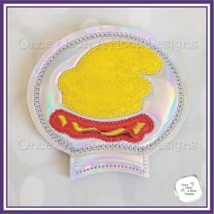 May include: A white, iridescent, round, embroidered patch with a yellow, embroidered, cartoon character wearing a red, embroidered hat. The patch has a silver, beaded border.