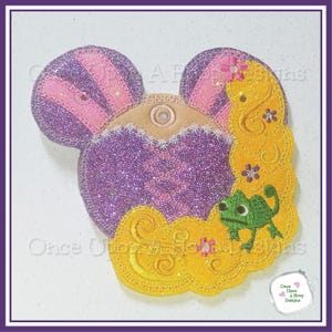 May include: Purple and pink glitter fabric Mickey Mouse ears with a yellow and gold glitter fabric Rapunzel hair design. A green chameleon is on the bottom of the hair design. The text "Once Upon A Hoop Designs" is on the image.