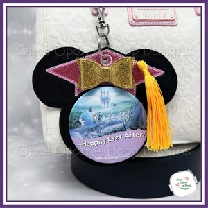 May include: Black felt Mickey Mouse ears with a pink and gold graduation cap, a yellow tassel, and a round button featuring Cinderella's carriage and Cinderella Castle. The button has the text "...Happily Ever After!" and "Walt Disney World".