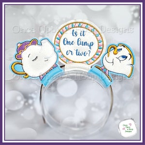 May include: A blue headband featuring a white teapot and cup, both with embroidered faces. The headband also has a round, pink and blue circle with the text "Is it One lump or two?" in gold embroidery.