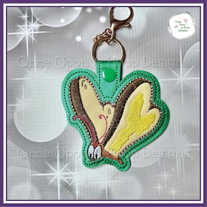 Può includere: Portachiavi a farfalla ricamata con bordo verde, ali beige e marroni e un accento giallo. Il portachiavi ha un fermaglio color oro e un bottone a pressione verde. Il design è di Once Upon a Hoop Designs.