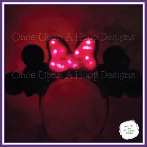 May include: A light-up Minnie Mouse ear headband with a bright pink bow and black ears. The bow has white polka dots. The text "Once Upon A Hoop Designs" is visible. The headband is set against a red background.