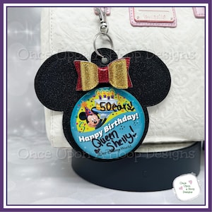 May include: A black felt Mickey Mouse ear keychain with a red and gold bow. A round blue button with a picture of Mickey Mouse celebrating his 50th birthday is attached to the keychain. The button says "50 ears! Happy Birthday! Queen Shelly!" and "Walt Disney World."