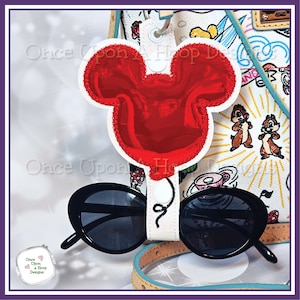 May include: A red Mickey Mouse shaped sunglasses holder with a white strap and black sunglasses. The holder is attached to a white bag with a colourful cartoon design.