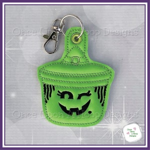 May include: A green felt witch's hat with a black smiling face and a winking eye. The hat has a loop for hanging and is attached to a silver key chain.