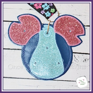 May include: A blue and pink glitter felt applique of a cartoon character with large ears. The applique is attached to a gold metal ring.