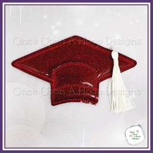 Op de afbeelding: Rode glitter-graduatiecap met een witte kwast. De dop is een plat, tweedimensionaal ontwerp. De tekst "Once Upon A Hoop Designs" is zichtbaar op de achtergrond.