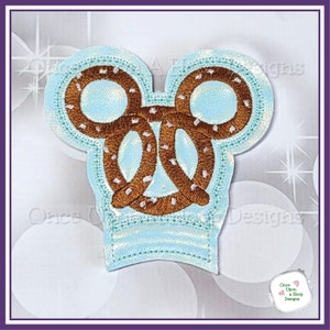 May include: A light blue embroidered patch shaped like Mickey Mouse ears with a brown pretzel design in the center.