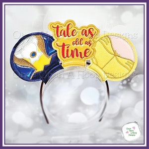 Puede incluir: Un par de orejas de ratón amarillas y azules con un diseño bordado en oro y rosa. Las orejas tienen el texto "Tale as old as time" en la oreja superior.