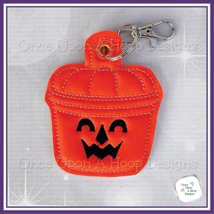 May include: Orange felt pumpkin bucket with a black jack-o'-lantern face. The bucket has a silver metal key ring attached.