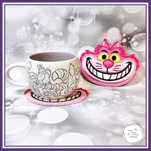 May include: A white ceramic mug featuring a black line drawing of the Cheshire Cat and other cats from Alice in Wonderland. The mug is resting on a pink and white coaster with a Cheshire Cat design. A separate pink and white coaster with a Cheshire Cat face is also pictured.