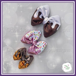 May include: Three handmade fabric hair bows with a dessert theme. The first bow is brown with white icing and sprinkles. The second bow is pink with white icing and colorful sprinkles. The third bow is orange and brown with a waffle pattern.